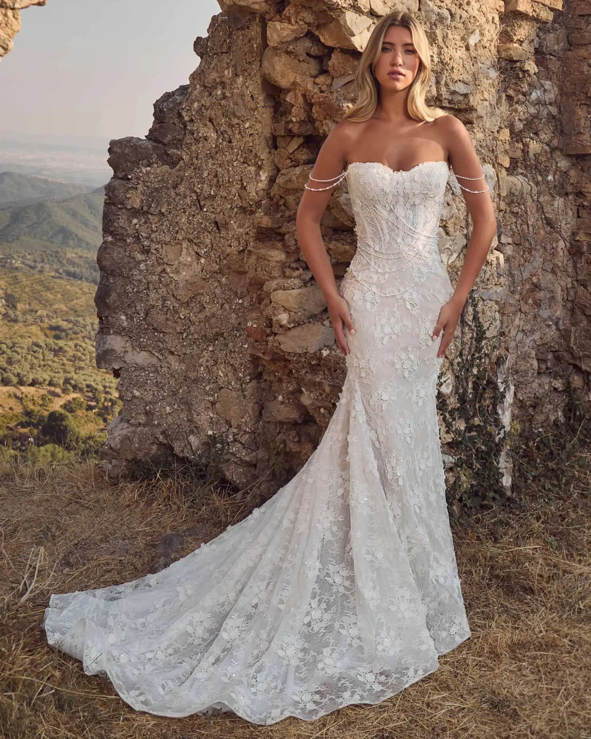 model is wearing a strapless fit and flare wedding dress with pearls as off the shoulder straps